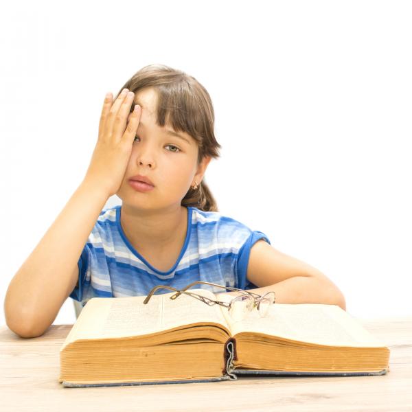 Child covering eye, with glasses lying on top of book
