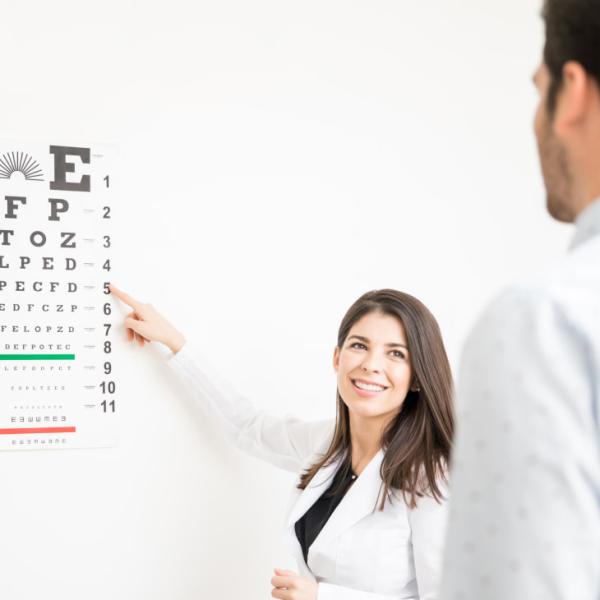 Una oculista apunta a una tabla optométrica frente a un paciente.