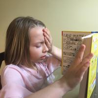 Girl reading book, with hand over one eye