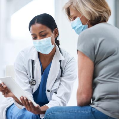 Foto de una doctora usando una tableta durante una consulta médica con una mujer adulta mayor.