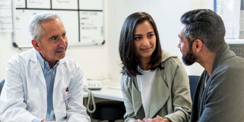 An image of a doctor and a couple talking in a doctors office