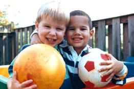 2 young boys hold balls and smile at the camera