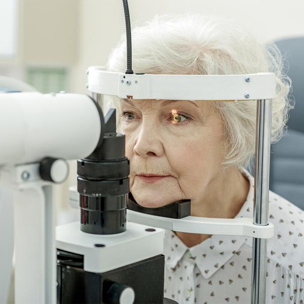An elderly woman has her eye examined using a slit lamp