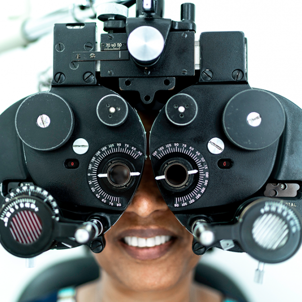 A woman looking at the camera through eye test equipment that's used during an eye exam.