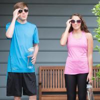 Two people with sunglasses stand in front of bench with work out clothes and water bottles